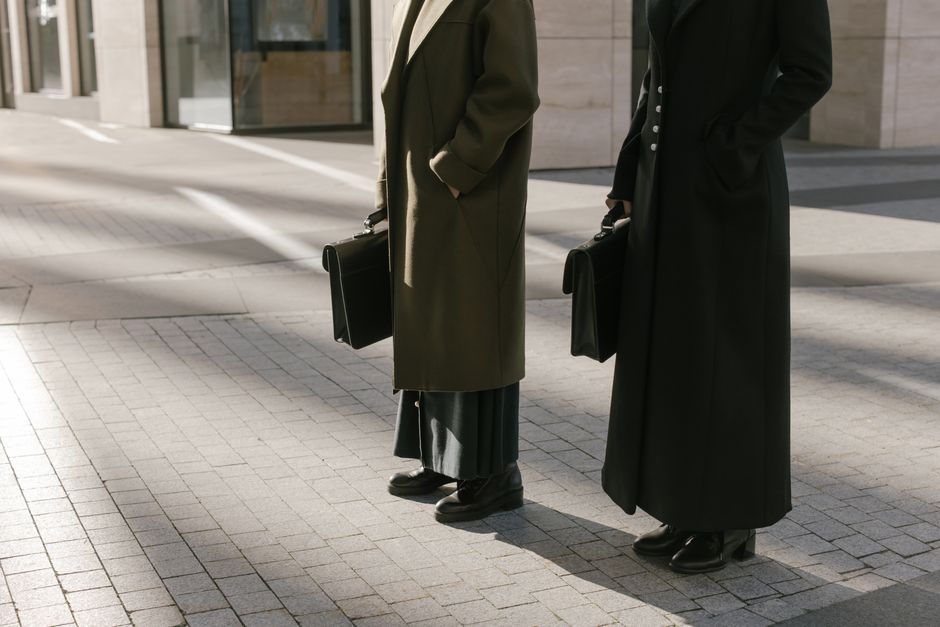 Two business professionals standing outdoors with briefcases, exuding elegance and professionalism.
