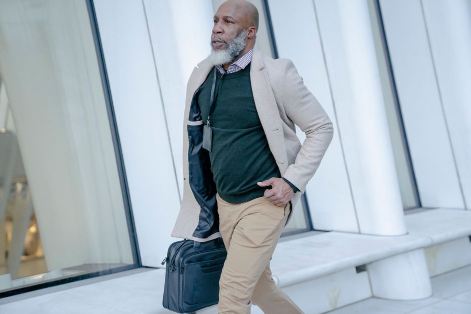 Confident bald man in a suit walking outdoors with a bag, exuding style and professionalism.