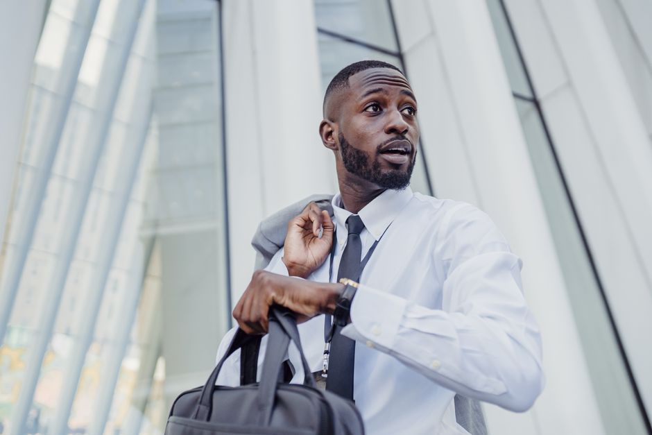 A professional businessman with a bag adjusting his tie outdoors.
