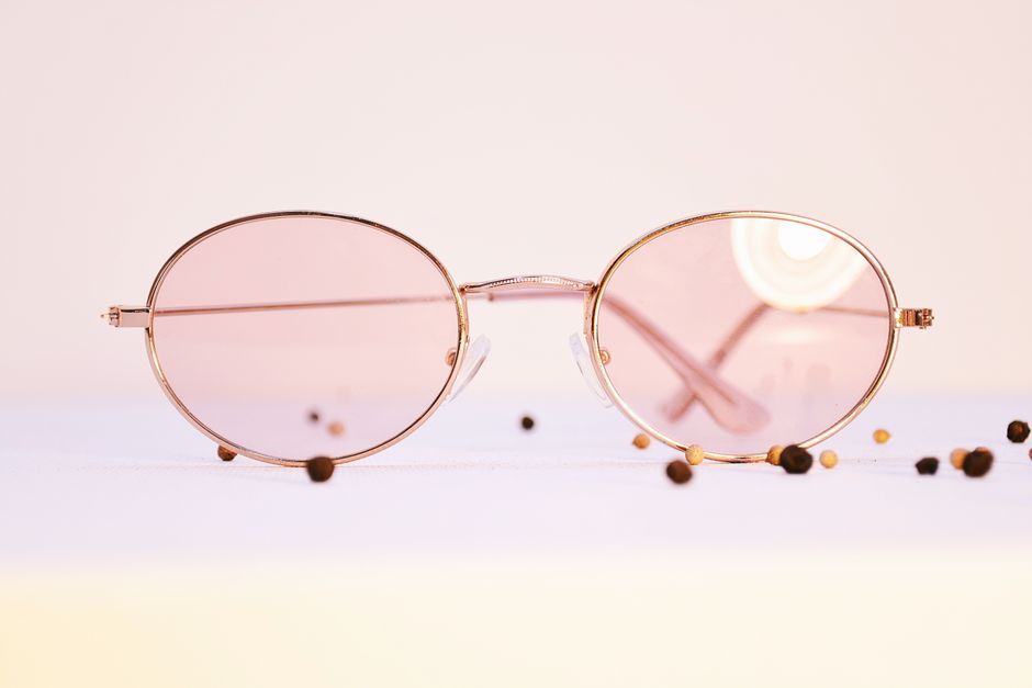 Elegant round sunglasses with pink lenses on a minimalist surface, surrounded by peppercorns.