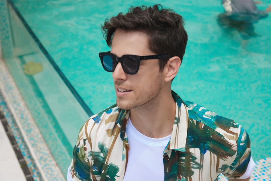 A fashionable man wearing sunglasses enjoys a sunny day by the pool, showcasing summer style.
