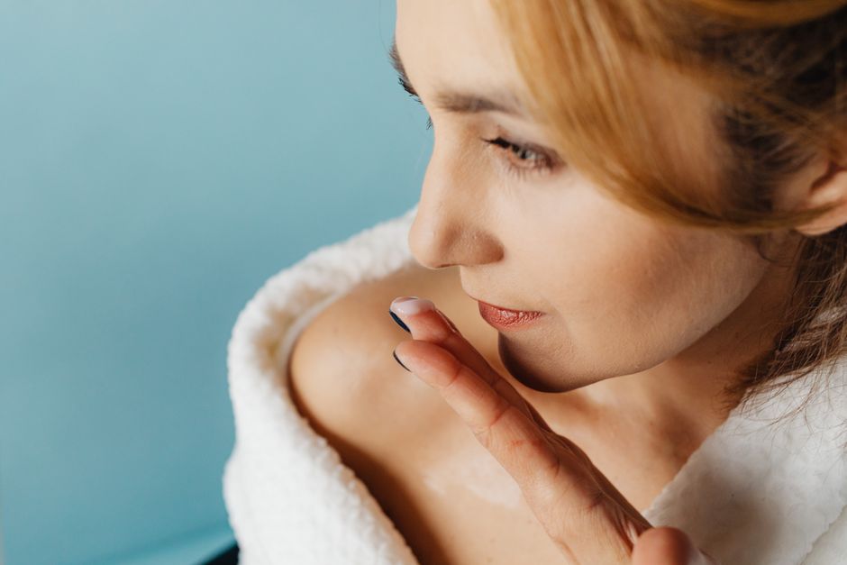 Close-up of a woman applying skincare cream while wearing a bathrobe, highlighting self-care routine.