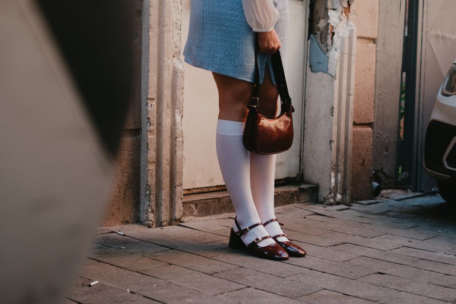 Fashionable woman in knee-high socks and stylish outfit holding a handbag on a city street.
