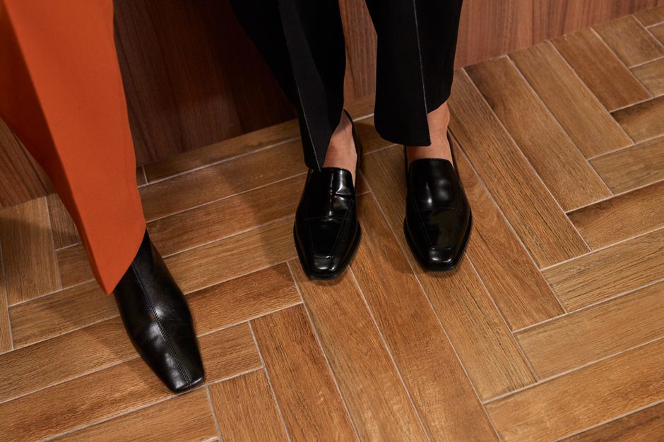 Elegant black shoes and orange pants on a stylish wooden herringbone floor.