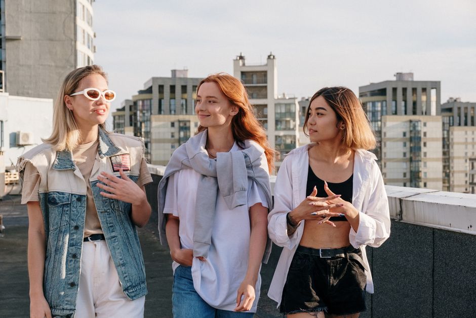 Three young women enjoy a sunny day on a rooftop, depicting friendship and urban lifestyle.