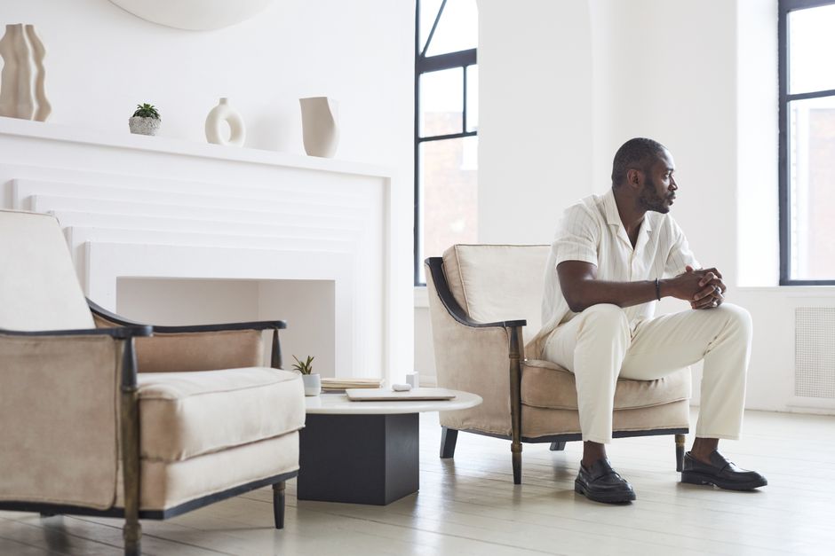 A thoughtful man sits in a modern, minimalist living room, exuding elegance and depth.