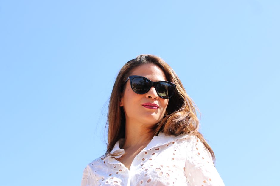 A stylish woman wearing sunglasses enjoys a sunny day outdoors, exuding confidence and elegance.