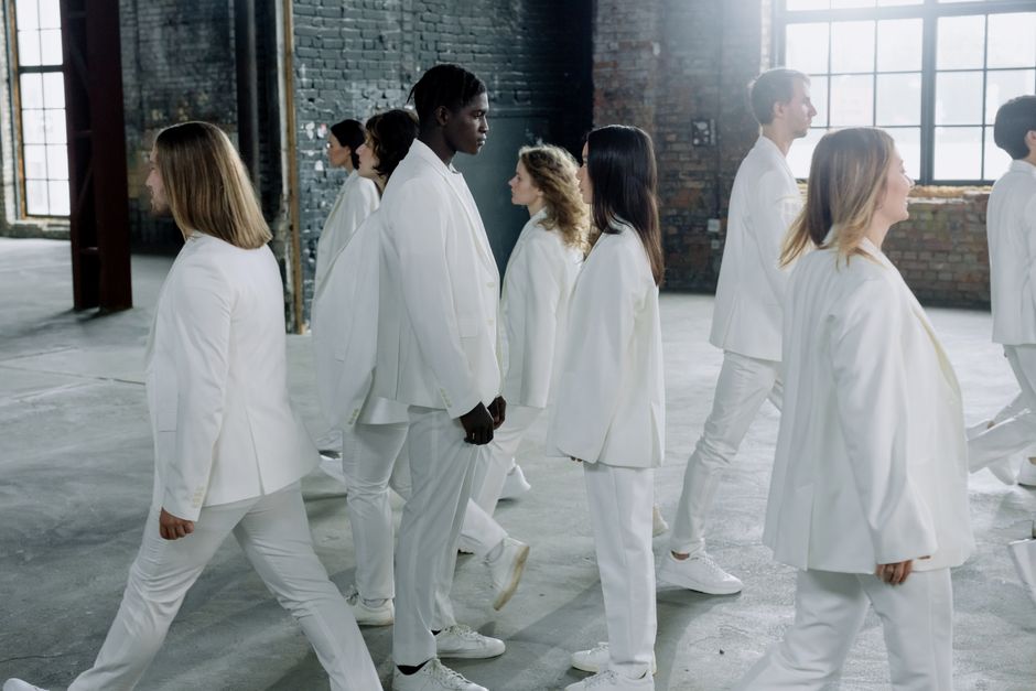 A diverse group of people in matching white outfits walking indoors, exuding unity and harmony.