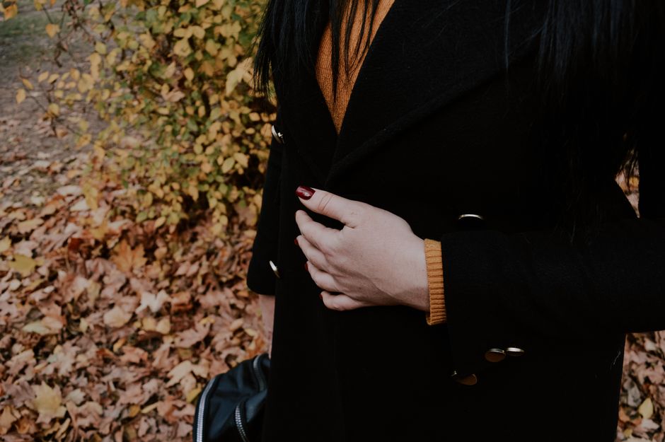 Woman with dark coat and painted nails standing near fall leaves in Kherson, Ukraine.