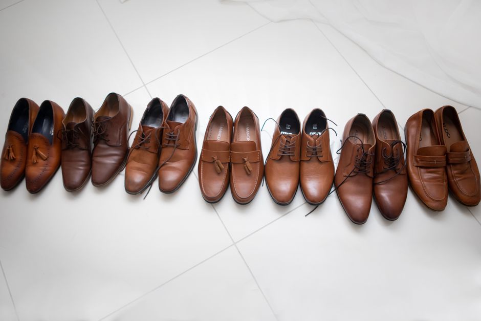 Diverse lineup of brown leather men's shoes displayed on a white tiled floor, emphasizing elegance and variety.