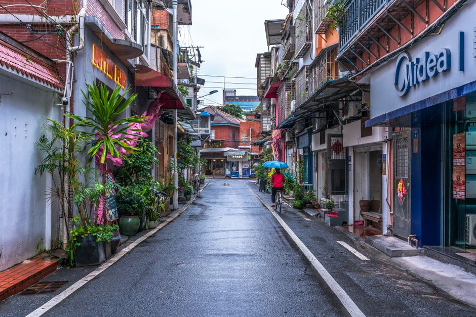A cyclist with an umbrella rides through a picturesque alleyway in a bustling city on a rainy day.