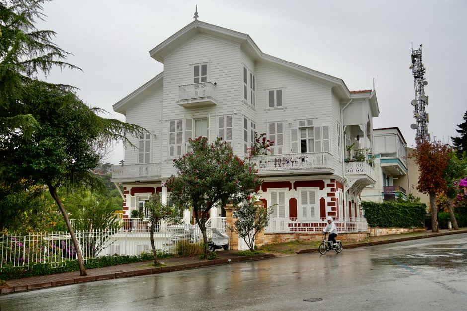 A beautiful white house with intricate details on a rainy street, surrounded by trees.