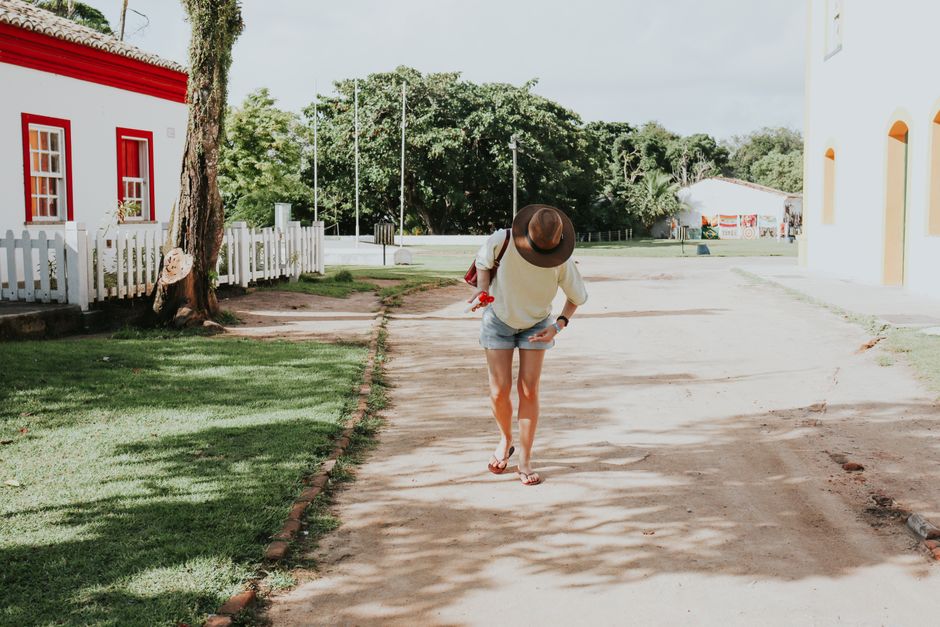 A woman in casual attire walks down a sunny street in Porto Seguro, Bahia, Brazil.