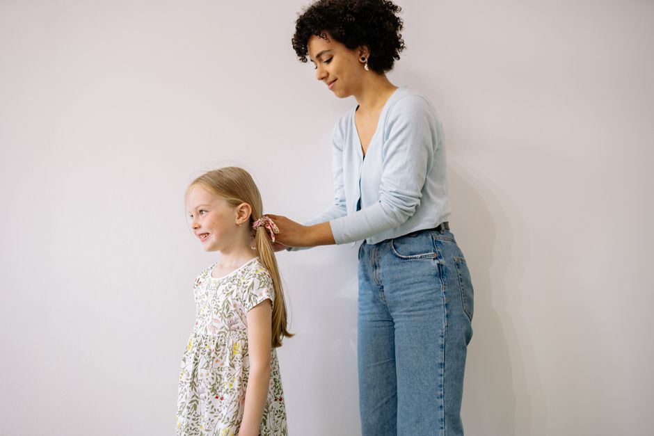 A joyful moment indoors as a mother braids her daughter's hair, showcasing love and togetherness.