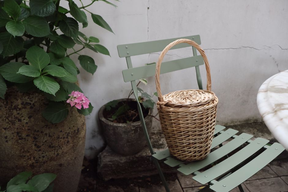 A wicker basket sits on a green chair in a serene NYC garden setting.