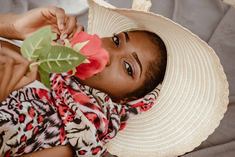 A stylish woman with a straw hat and scarf holds a rose with a serene expression.