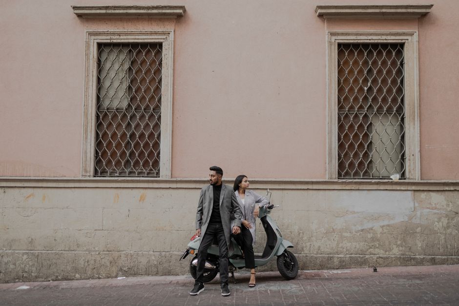 A fashionable couple leaning on a scooter against a vintage building facade, exuding urban coolness.