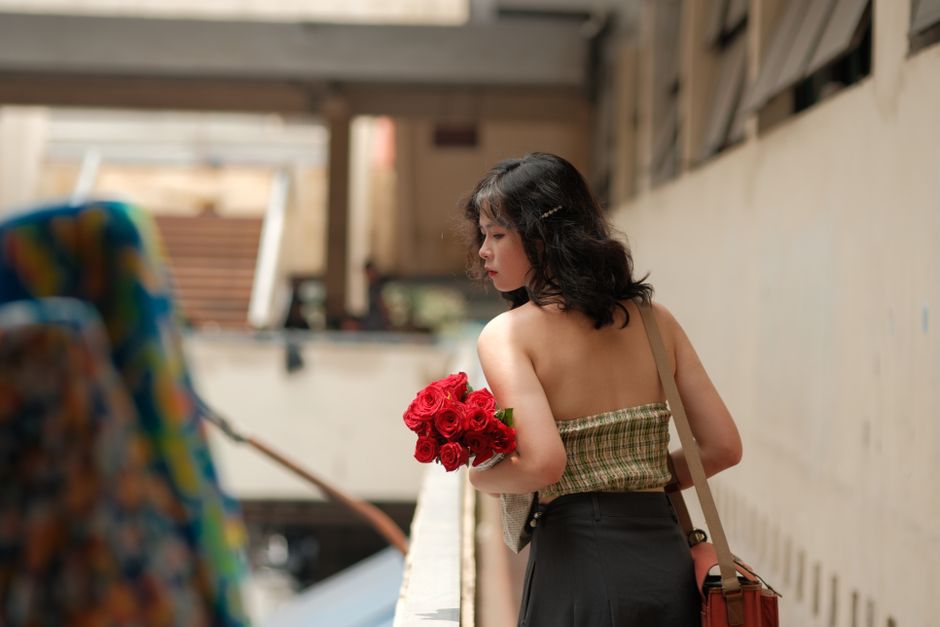 A woman in a strapless top holding red roses, walking indoors in a city area.